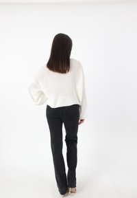 Losse witte gebreide trui met drop sleeves, gecombineerd met zwarte flare jeans. De outfit heeft een eenvoudig ontwerp zonder opvallende patronen.
