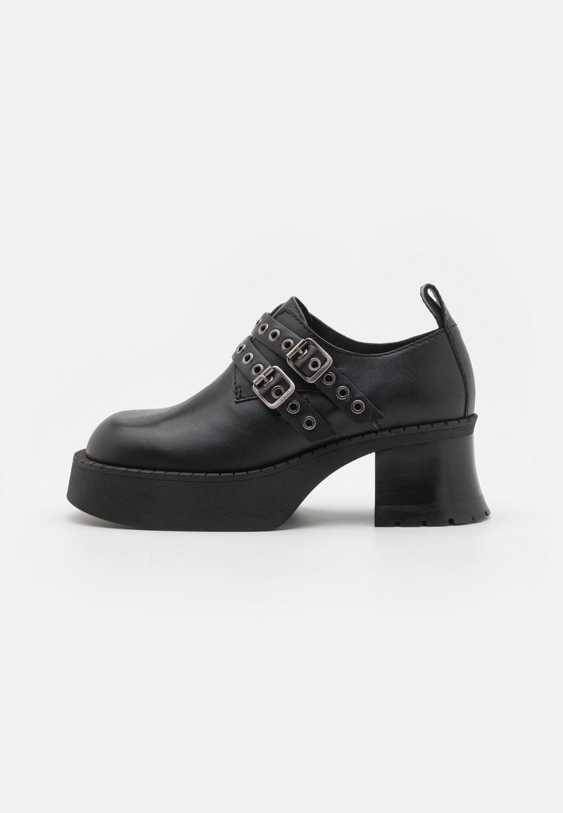 Black leather platform shoes with a wide, high heel. Features two silver buckle straps and rivet detailing around the ankle. Smooth texture.