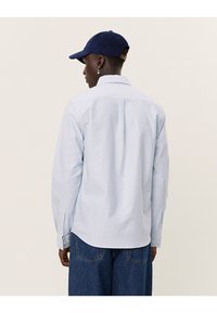 Lichtblauw en wit gestreepte blouse met een kraag, lange mouwen en knopdetails op de manchet, gezien van achteren.
