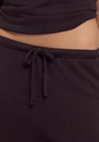 Musta neulepuku, jossa on kiristettävä vyötärö. Pehmeä materiaali ja rento istuvuus korostavat sileää kangasta ja minimalismia.