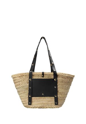 Bolso tote de paja tejido con bolsillo delantero de cuero negro y asas de cuero negro con tachuelas que se extienden por debajo del borde del bolso.