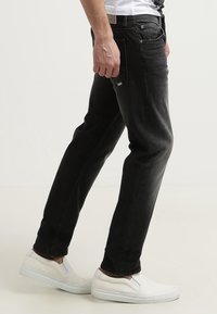 Černé džíny z denimu se střihem rovného řezu, s pěti kapsami a jemně vybledlou texturou. Kombinovány s bílými nazouvacími botami.