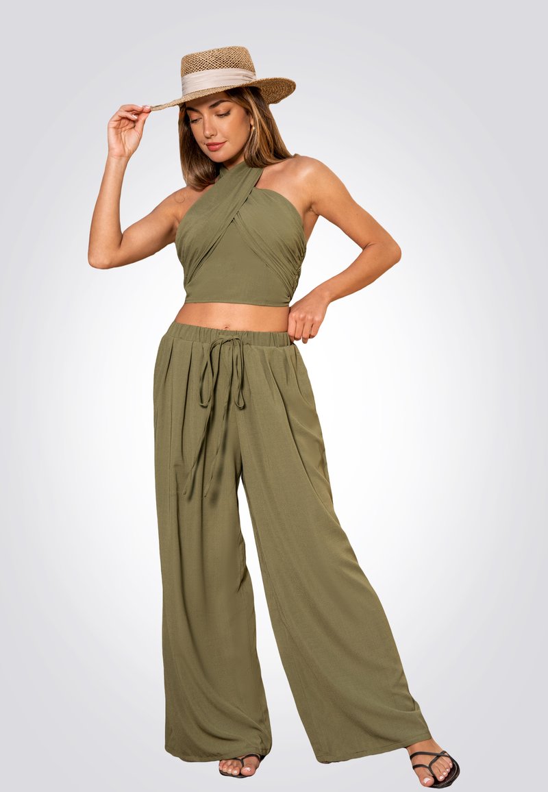 Conjunto de dos piezas en verde oliva que incluye un top corto con cuello halter y frente retorcido, y pantalones de pierna ancha con cintura atada. La modelo lleva un sombrero de paja.