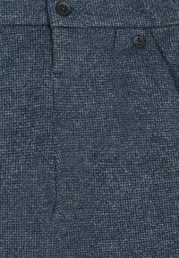 Tissu texturé bleu marine avec un motif tissé, comportant deux boutons noirs et une poche à rabat. Le matériau offre une apparence légèrement robuste.