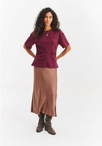 Bordowa bluzka z krótkim rękawem z subtelnym marszczeniem po bokach, połączona z brązową satynową maxi spódnicą i brązowymi zamszowymi kozakami za kolano.