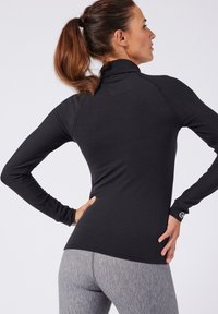 Zwarte top met lange mouwen en hoge kraag, slim fit en een gladde textuur, gecombineerd met nauwsluitende grijze legging. Logo op de mouw.
