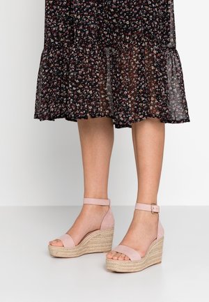 Sandały na koturnie z różowym zamszowym wierzchem, pasek na kostkę z klamrą i plecioną juteową podeszwą. Otwarty nos i widoczna teksturowana powierzchnia.