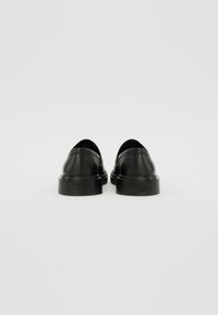 Chaussures noires en cuir à enfiler avec des bouts ronds et des semelles en caoutchouc basses. Surface texturée avec des détails de couture à l'arrière.