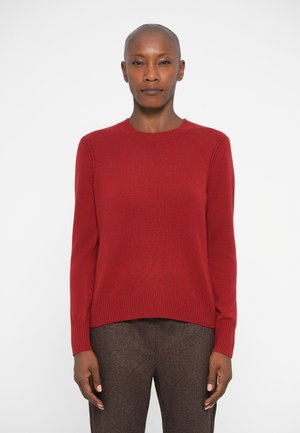 Rød strikket sweater med rund halsudskæring, ribbede manchetter og kant. Båret med teksturerede brune bukser, der har en glat overflade og en tætsiddende silhuet.