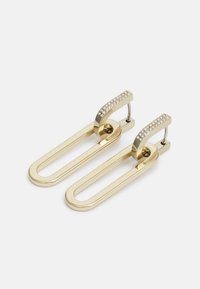 Des boucles d'oreilles en ton doré avec un design en forme de trombone, dotées d'un sommet incurvé orné de petits cristaux transparents pour une touche de détail.