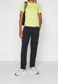 Hellgrünes kurzärmeliges T-Shirt, schwarze Cargo-Hosen mit Reißverschlüssen und hellgraue Sneaker mit orangen Akzenten. Lässiges Freizeitoutfit für draußen.