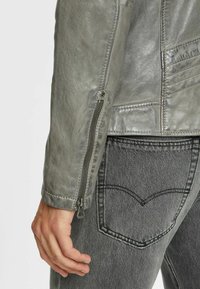 Grå læderjakke med lynlås i ærmerne og struktureret finish, parret med grå jeans, der har et tydeligt syet lomme-design.