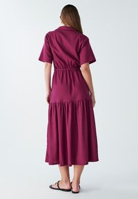 Bordo midi haljina s kratkim rukavima, stegnutim strukom i slojevitom suknjom. Izrađena od laganog materijala s glatkom teksturom.