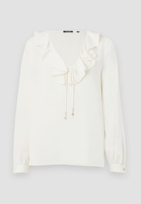 Blouse blanche à manches longues avec col en V à volants et lien orné de charms argentés, poignets boutonnés, et étiquette de marque au col.