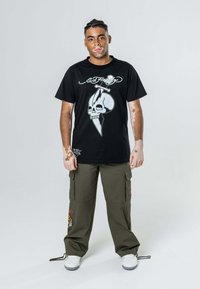 Czarna koszulka z krótkim rękawem z białą grafiką czaszki i sztyletu. Połączona z luźnymi oliwkowymi spodniami cargo, które są zarówno swobodne, jak i funkcjonalne.