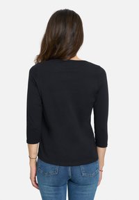 Camiseta negra de manga larga con escote redondo y diseño ajustado, combinada con vaqueros de mezclilla azul. Tejido suave con un corte sencillo.