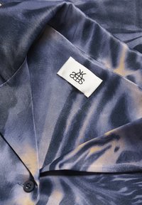 Satin shirt in donkerblauw en beige met een subtiel, abstract patroon. Voorzien van een notch-kraag en een ingenaaid label met zwart logo.