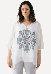 Blusa bianca trasparente con scollatura a V e maniche fluide, caratterizzata da un colorato motivo floreale e paisley in rosa, verde e nero.