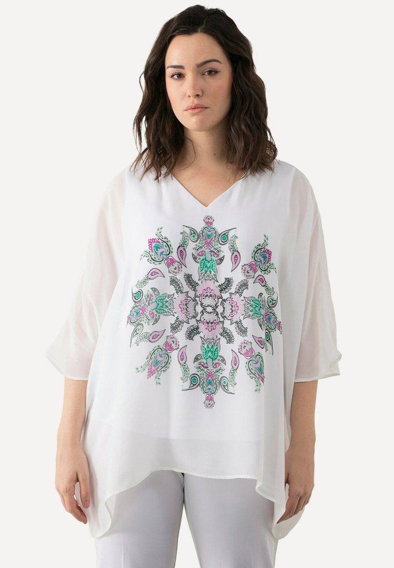 Blusa bianca trasparente con scollatura a V e maniche fluide, caratterizzata da un colorato motivo floreale e paisley in rosa, verde e nero.
