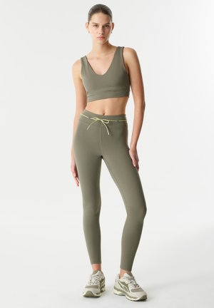 Ensemble de sport vert olive composé d'un crop top à col en V et de leggings taille haute, avec un cordon de serrage et un tissu lisse et extensible.