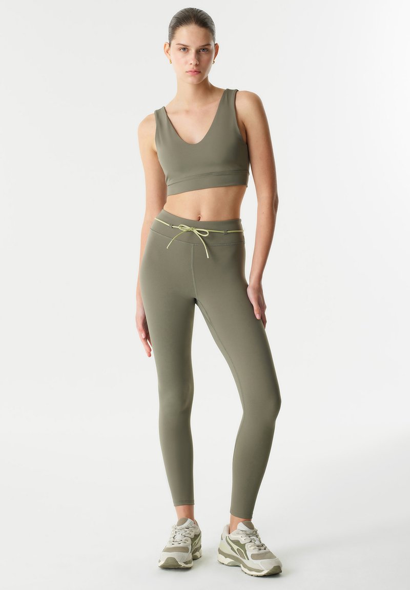 Completo sportivo verde oliva composto da un crop top con scollatura a V e leggins a vita alta, dotati di cordoncino e realizzati in tessuto morbido ed elasticizzato.