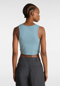 Ljust blå cropped tanktop med rund halsringning och ärmlös design, tillsammans med mörkgrå byxor med bakfickor. Mjuk textur.