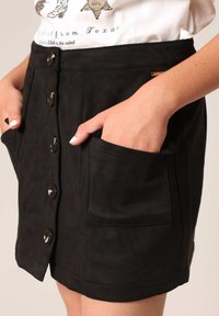 Zwarte suède rok met een knoopsluiting aan de voorkant, zijzakken en een gladde textuur. Eenvoudig ontwerp met een strakke afwerking.