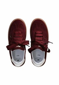 Un paio di sneakers bordeaux in suede con lacci larghi e suole in gomma, viste dall'alto su uno sfondo bianco.