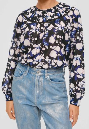 Schwarzbluse mit floralen Mustern in Blau- und Rosatönen, mit gerafftem Ausschnitt und langen Ärmeln, kombiniert mit hellblauen Jeans.