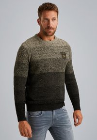 Gebreide sweater met een verloop van lichtgroen naar zwart, met een textuurpatroon en een zwarte patch met gele accenten.