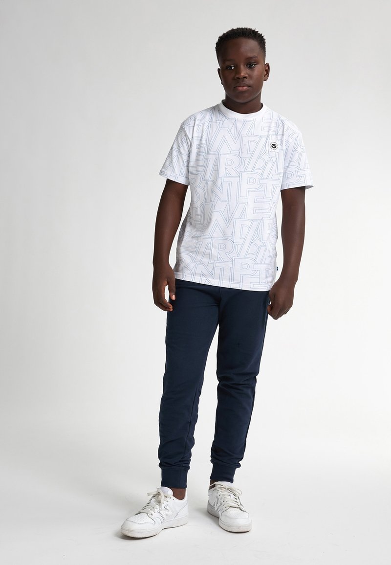 Camiseta blanca de manga corta con un patrón geométrico repetido, combinada con pantalones deportivos azul marino y zapatillas blancas con cordones.