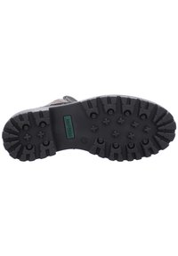 Suela de goma negra con profundas ranuras para tracción. Presenta una etiqueta de logo verde y patrones en relieve para agarre. Diseñado robusto y texturizado.