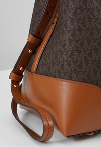 Gros plan sur un sac à main en cuir marron avec un motif sombre, des sangles réglables et des coutures visibles.