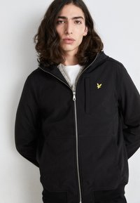 Hanorac negru cu fermoar, dotat cu un buzunar frontal. Are un logo brodat galben pe piept, o glugă căptușită și manșete și tiv cu nervuri.