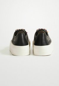 Baskets en cuir noir avec des semelles compensées blanches. La vue arrière montre des accents en perles colorées sur le talon et un marquage en relief sur les côtés.