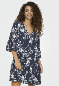 Robe à imprimé floral en marine avec des motifs botaniques blancs. Elle présente un décolleté en V et des manches volantes, fabriquée à partir d'un tissu léger.