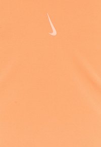 Camiseta de algodón Nike en naranja claro con un pequeño logo pálido en el pecho. Textura suave, con mangas cortas y un cuello redondo.