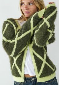 Fuzzy oliwkowy kardigan z limonkowymi wzorami w romby, o luźnym kroju, z prążkowanym wykończeniem rękawów i miękką teksturą.