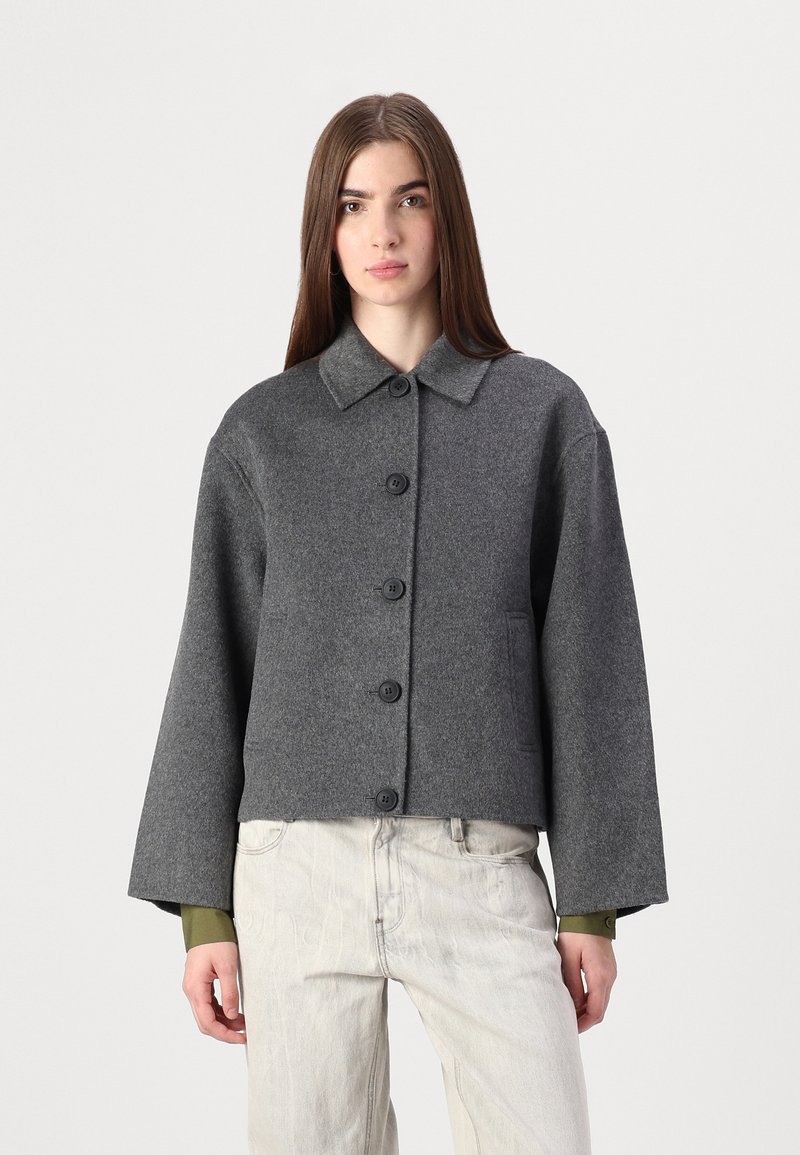 Veste courte en mélange de laine grise avec un col, six boutons et deux poches latérales ; possède des manches larges et une texture douce.