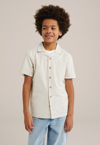 Camicia a maniche corte, color crema, con sottili righe verticali, colletto a punta, bottoni in legno e una tasca sul petto. Vestibilità casual.