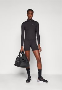 Svart treningsantrekk med langermet topp, shorts og svarte joggesko. Bærer en svart treningsbag. Har minimalistisk design og PUMA-merke.
