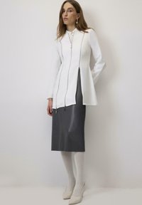 Balta jaketi ar garām piedurknēm un priekšējiem rāvējslēdzējiem, kombinēta ar elegantu pelēku svārku. Apģērbs izceļas ar gludu tekstūru un minimālistisku dizainu.