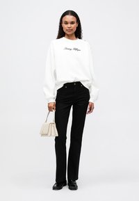 Valkoinen huppari, jossa on "Tommy Hilfiger" -logo, mustat korkeavyötäröiset farkut, beige käsilaukku ja mustat kengät. Sileä kangas ja rento malli.