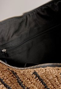 Borsa intrecciata in paglia color marrone chiaro con dettagli neri, dotata di interno in tessuto nero e tasca con cerniera per una conservazione sicura.