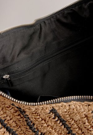 Heledatpruunist kootud heina käekott mustade aktsentidega, millel on musta kangaga sisemine osa ja tõmblukuga tasku turvaliseks hoiustamiseks.