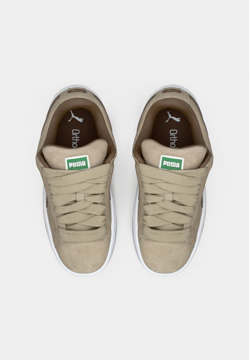 Zapatillas deportivas de ante beige con una suela de goma blanca redonda, cordones planos, etiqueta de logo verde en la lengua, y una plantilla acolchada marrón.