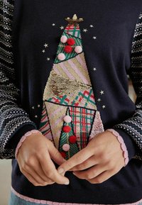 Gestrickter Pullover mit einem mehrfarbigen Pailletten-Weihnachtsbaum-Design, verziert mit Bommel und Sternakzenten auf einem marineblauen Hintergrund.