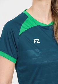 Præstationssports skjorte i teal med grønne detaljer, lavet af glat stof. Har et subtilt struktureret mønster og hvidt 'FZ'-logo.