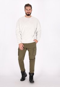 Grijze sweatshirt, olijfgroene cargobroek met zijzakken en zwarte veterschoenen. Slim-fit ontwerp met een gladde textuur en minimale details.
