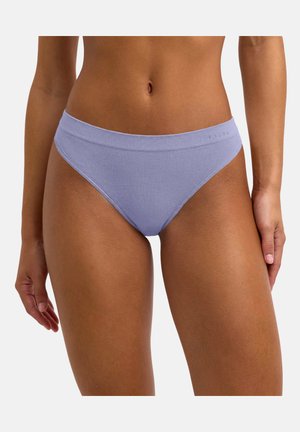Femme portant un bas de bikini côtelé violet clair, vue de la taille au milieu de la cuisse sur fond uni.